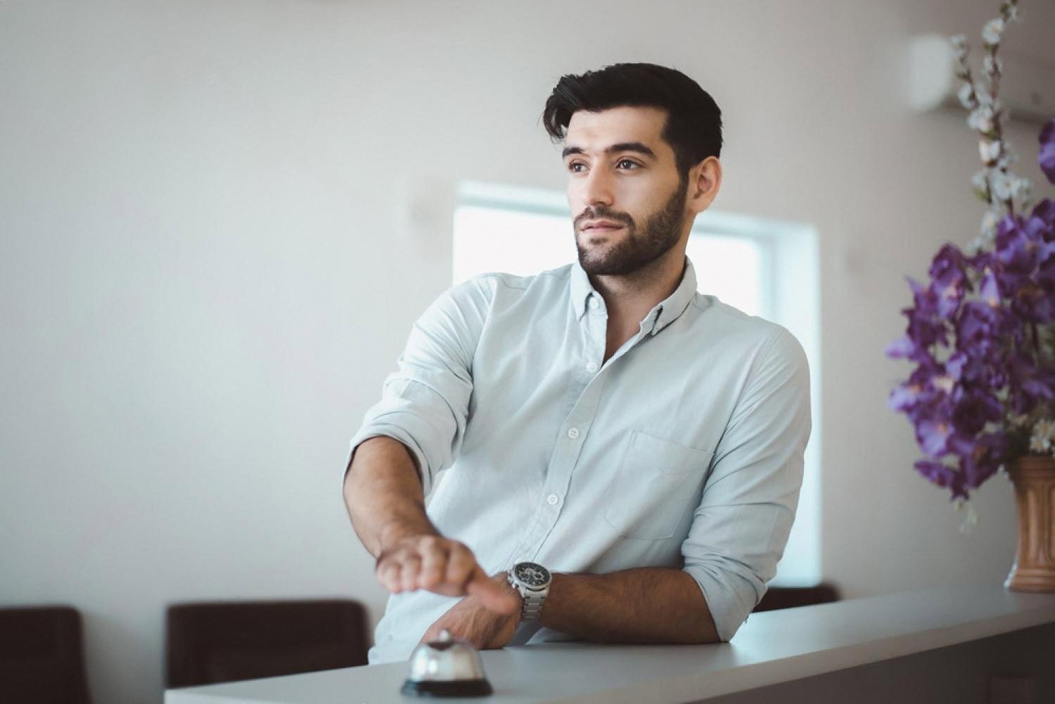 Hotel guest standing at a reception counter ringing a service bell