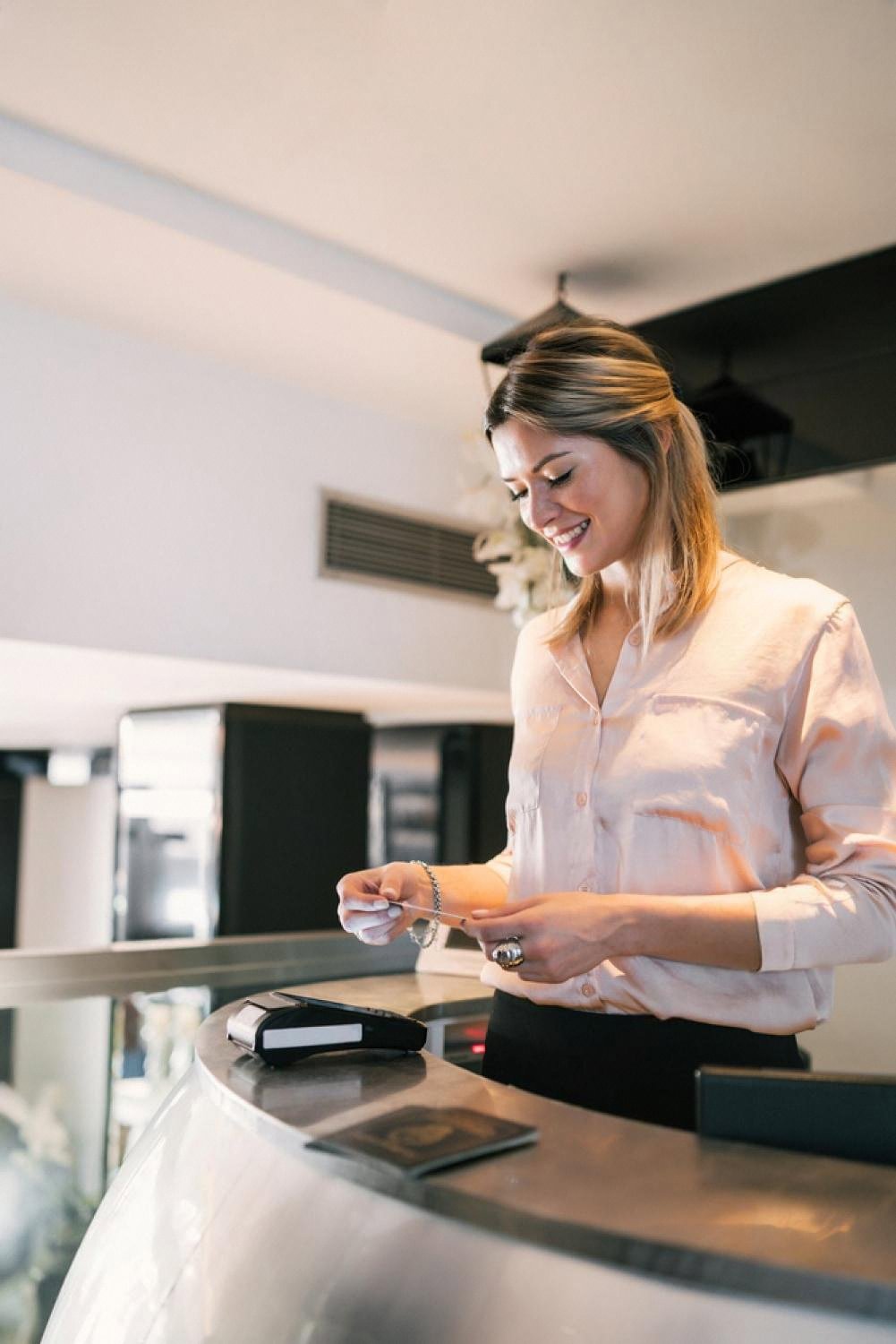 Smiling hotel receptionist processing a payment at a modern front desk